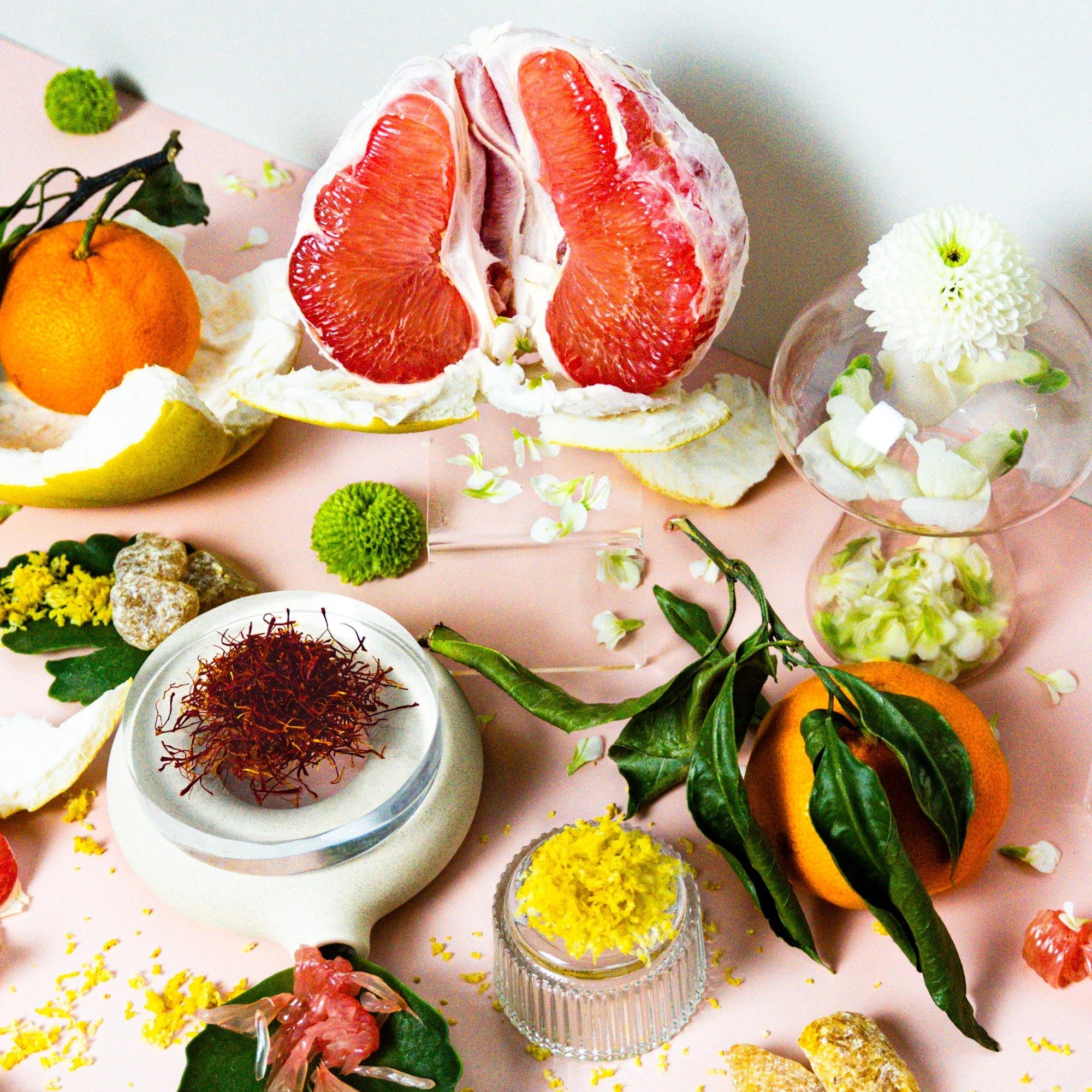 An assortment of citrus fruits including grapefruits and oranges, alongside flowers and what appears to be a small container of fragrance oil.