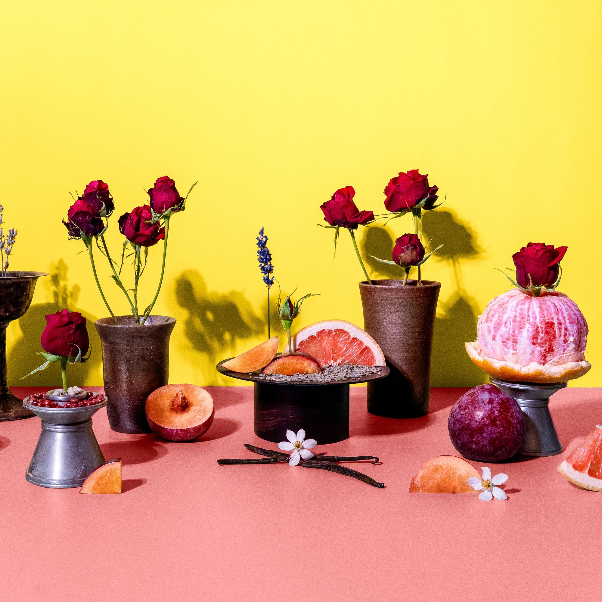 Decorative setup with flowers, fruits, and small tables against a yellow and pink background