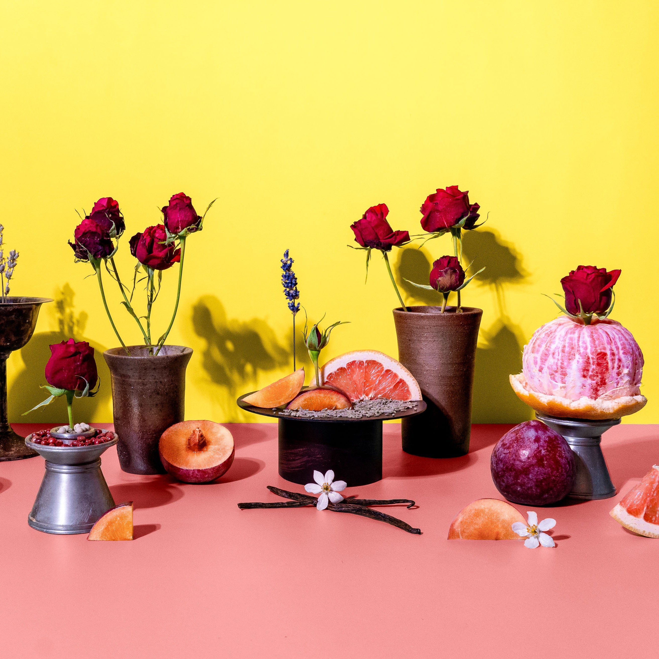 Decorative setup with flowers, fruits, and small tables against a yellow and pink background