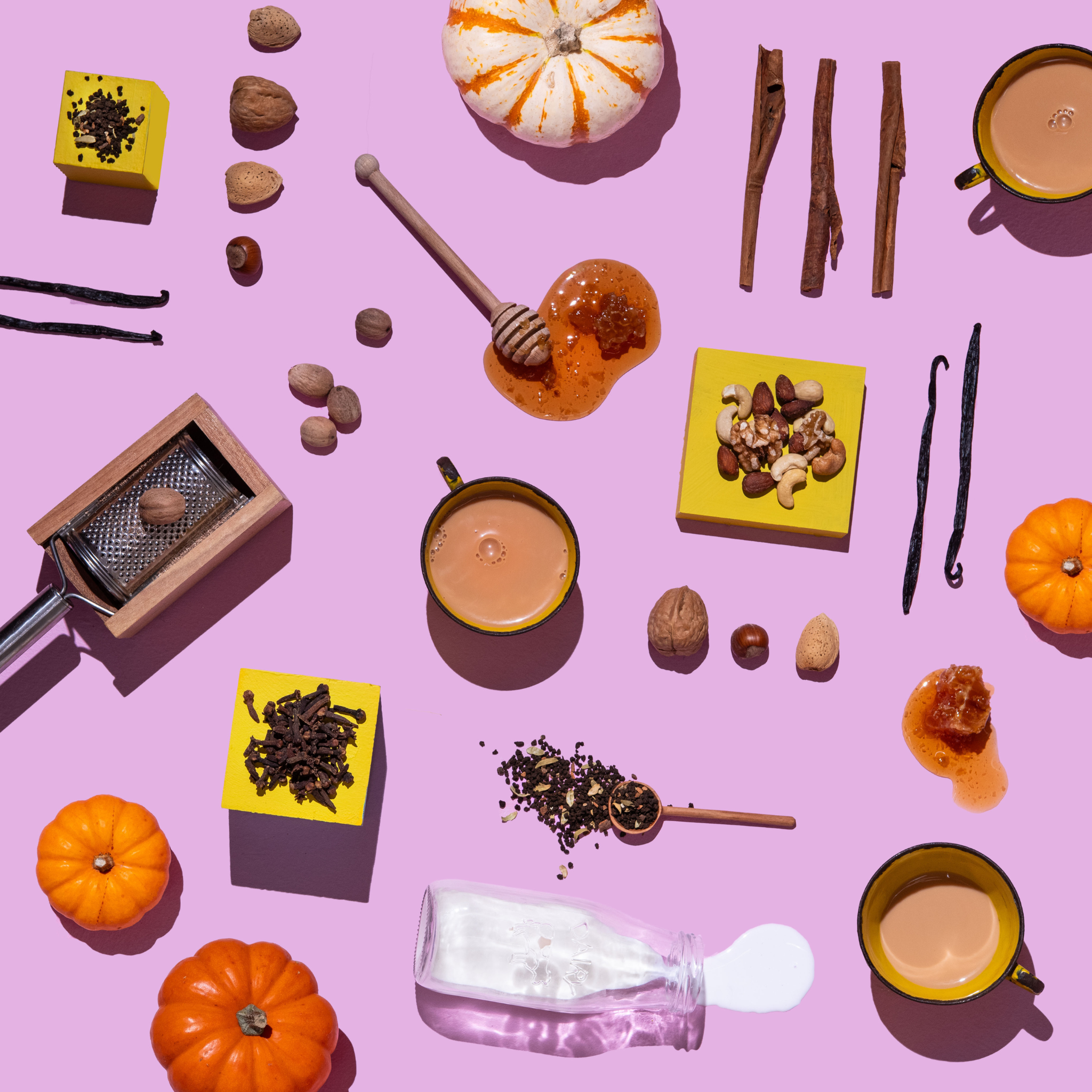 Spice mix, pumpkins, cinnamon sticks, and other fall-themed items on a pink background
