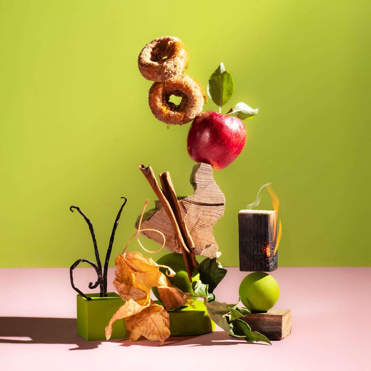 Decorative arrangement with apples, donuts, and candles on a pink surface against a green background