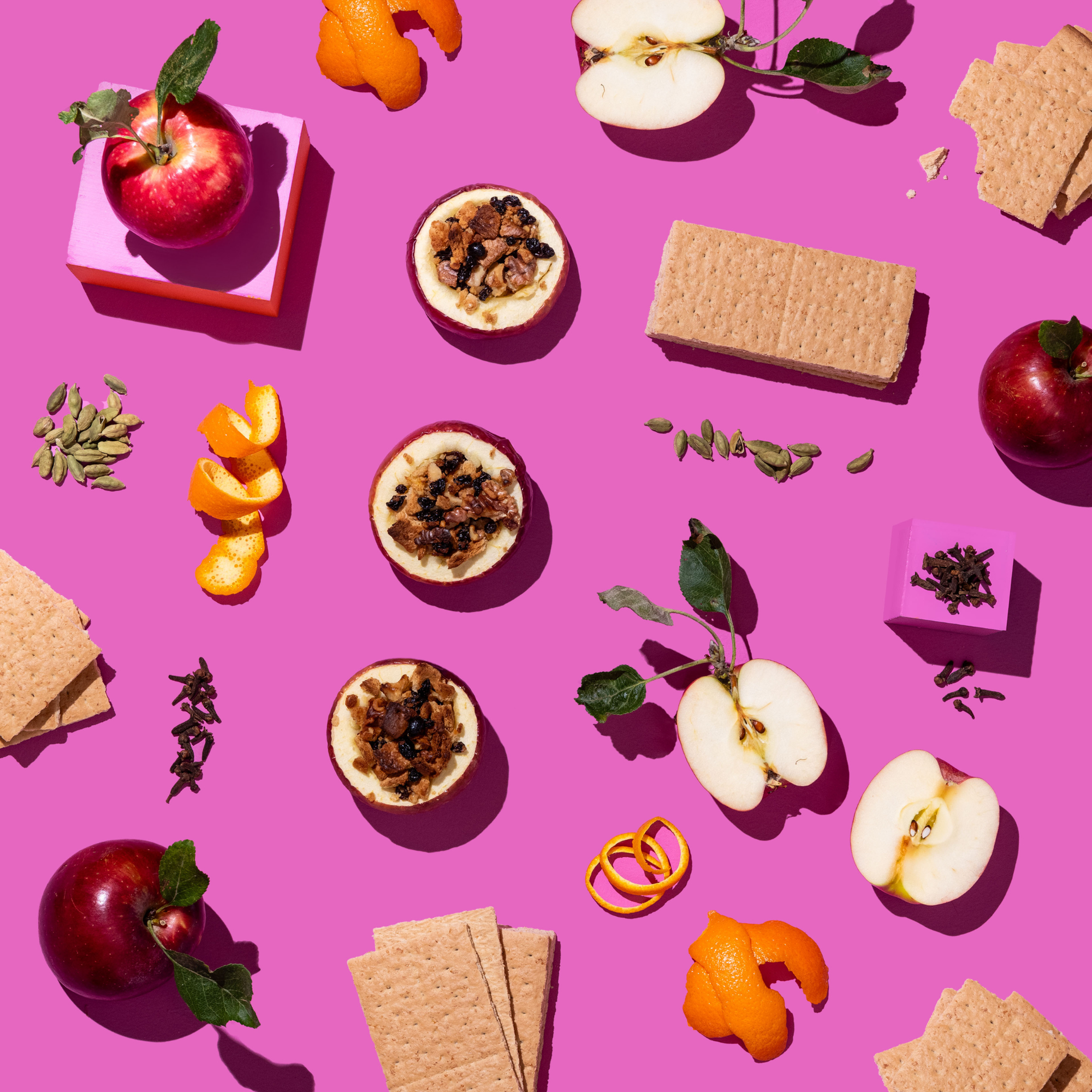 Assorted food items including apples, cookies, and spices on a pink background