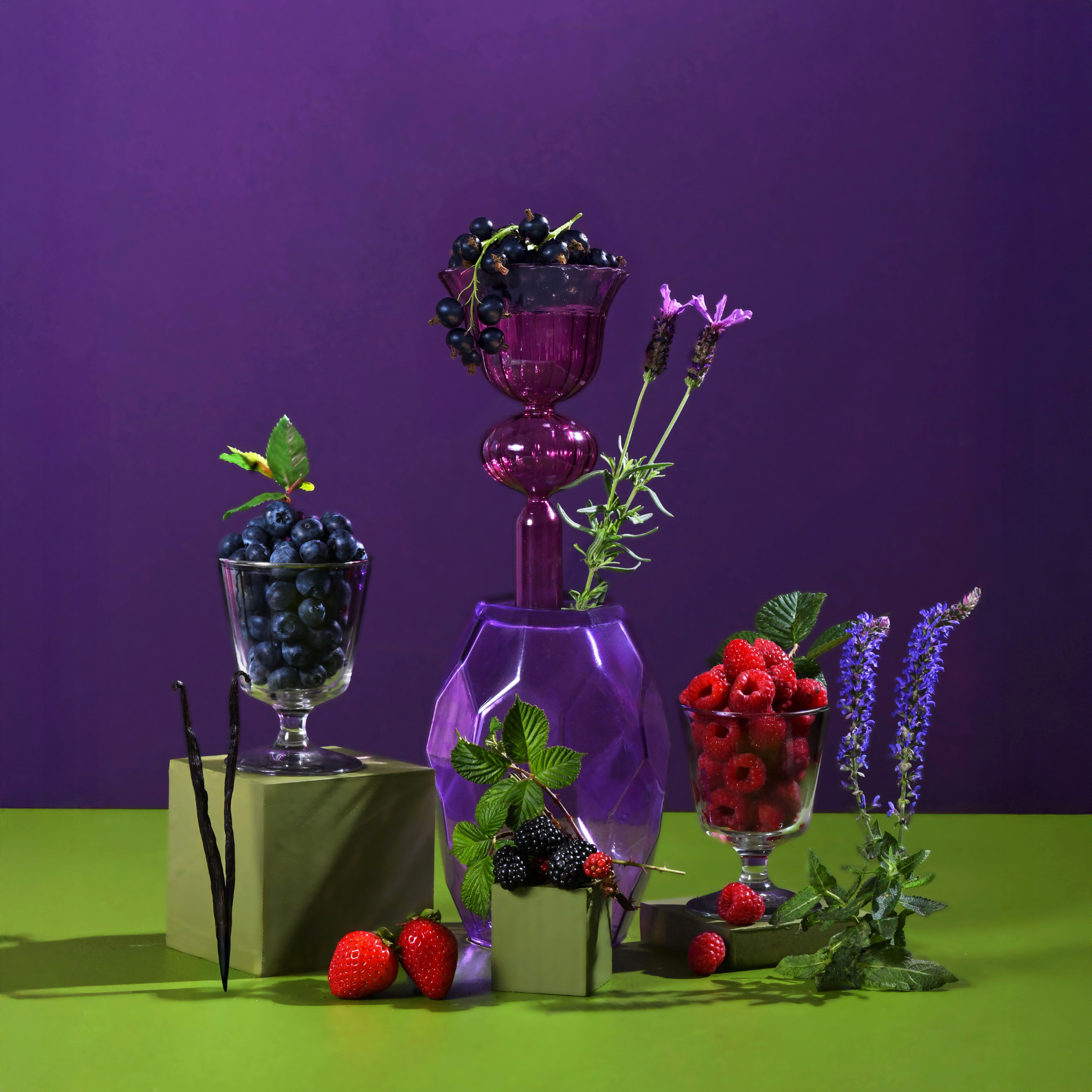 Decorative setup with purple glass vase, berries, and flowers on a green surface against a purple background
