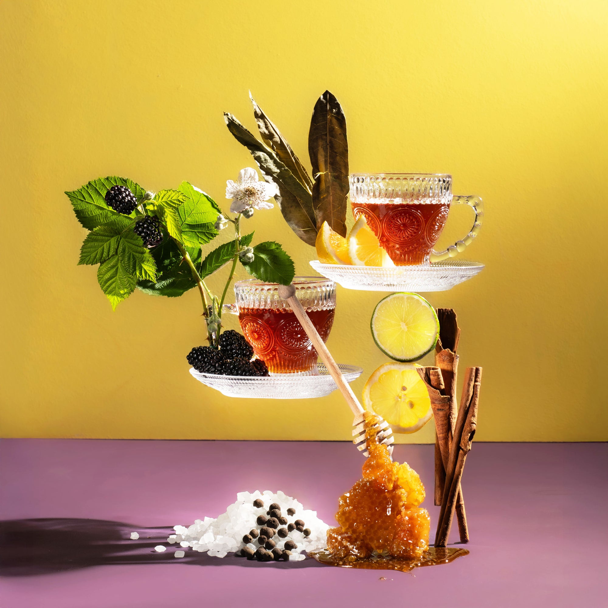 Tea setup with cups, lemon slices, and garnishes on a yellow and purple background