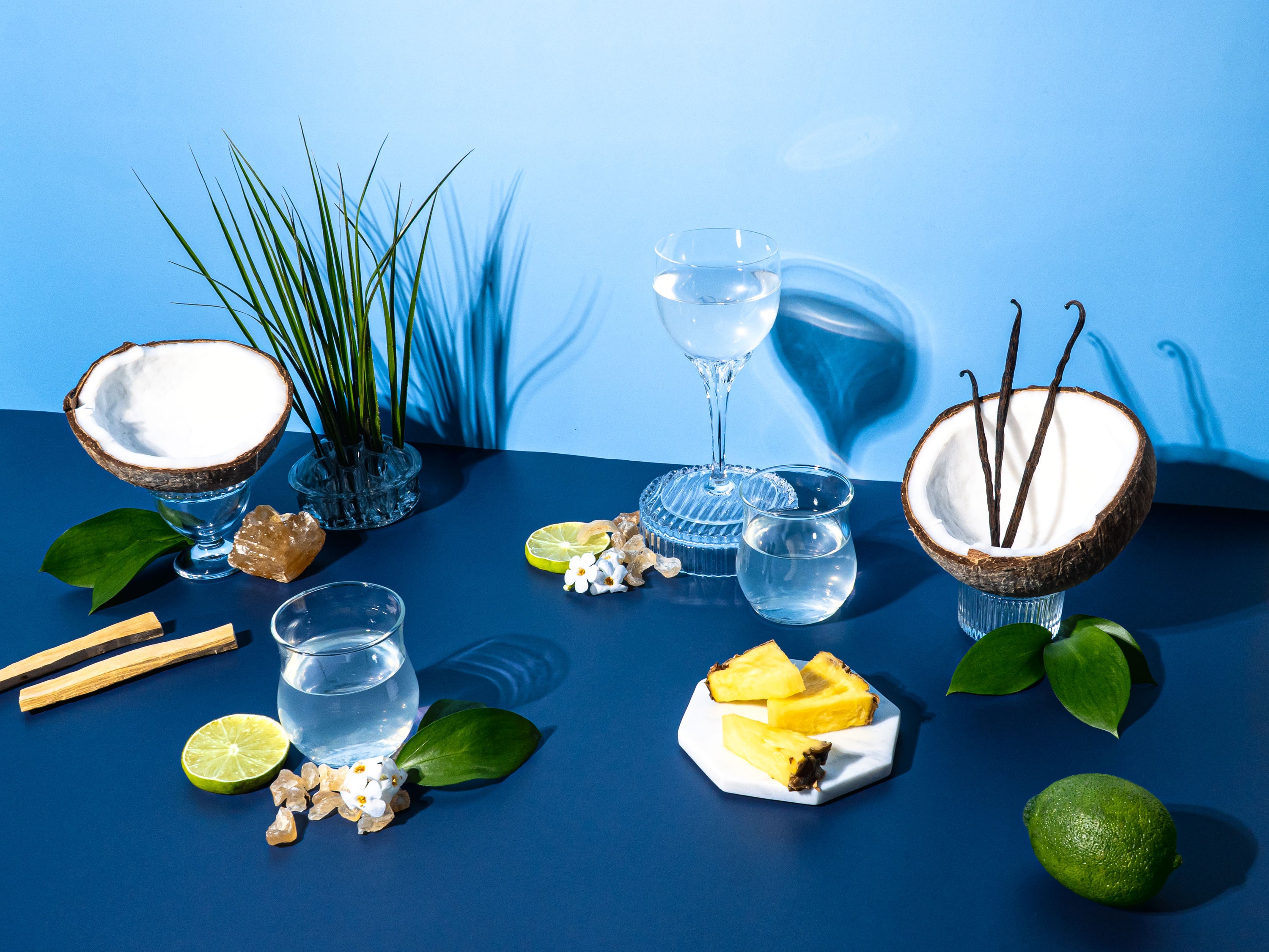 Cocktail setup with glasses, fruits, and garnishes on a blue surface