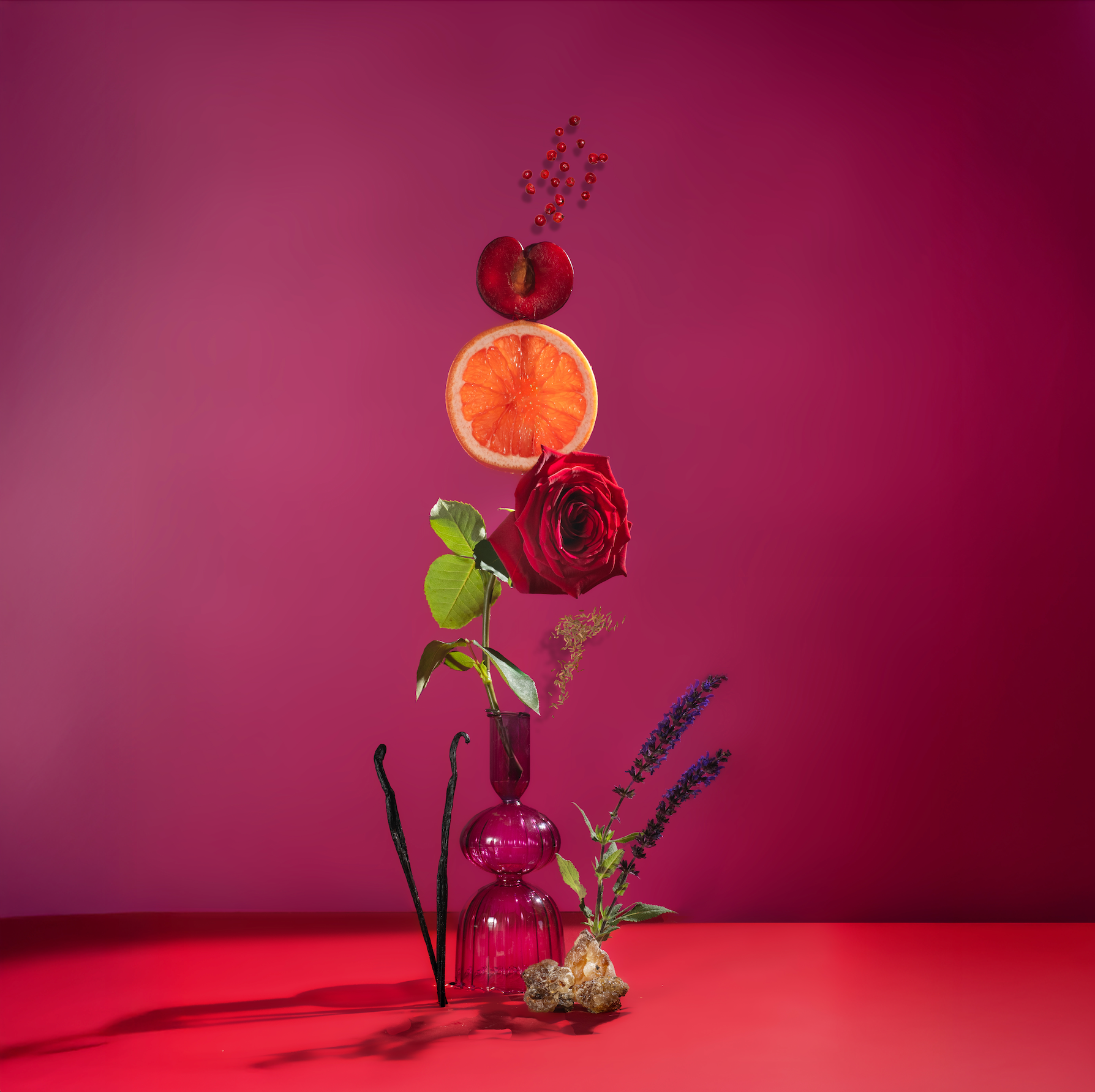Vase with flowers and fruits on a red surface against a pink background
