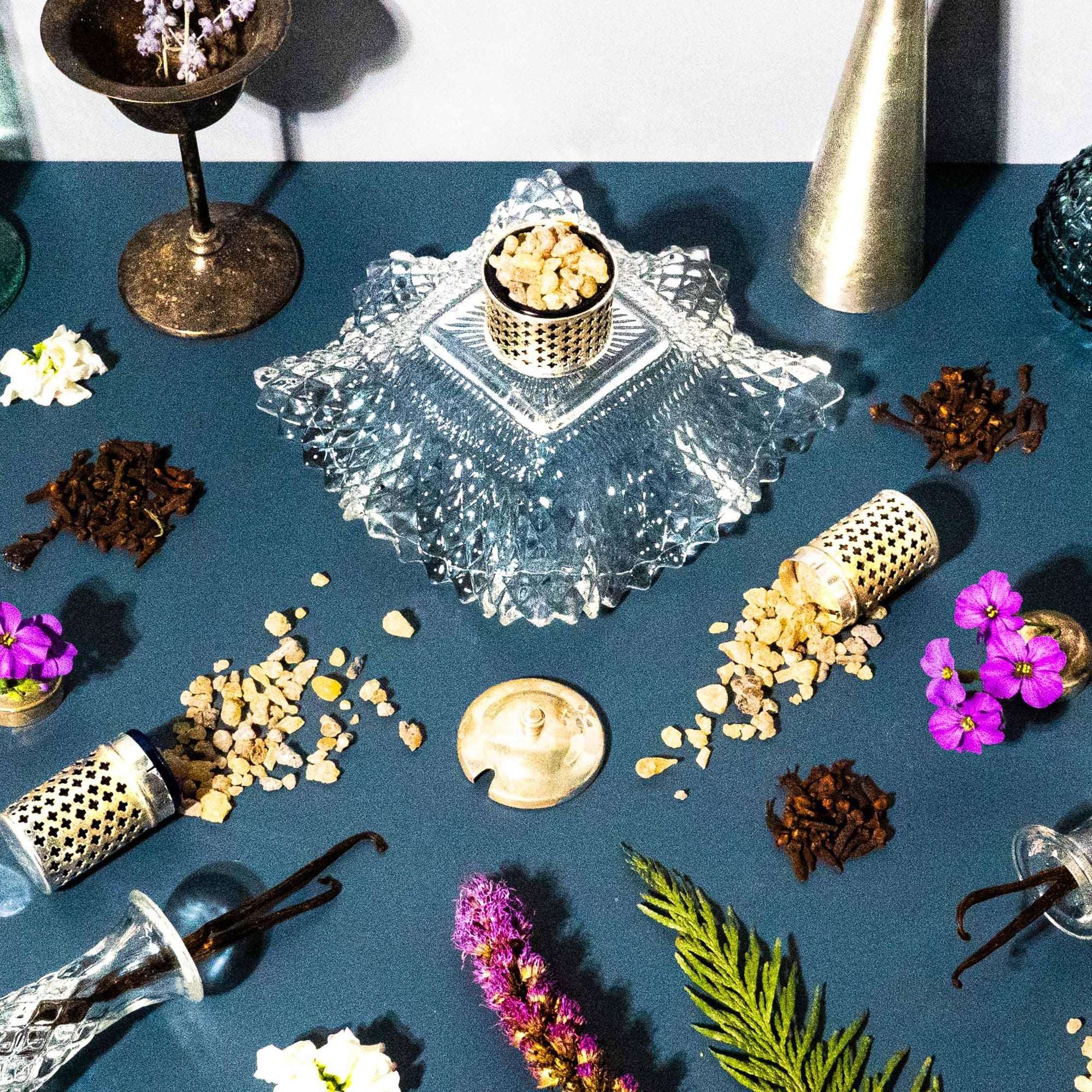 An assortment of fragrance oils and ingredients displayed on a blue surface, including patchouli, frankincense, and myrrh.