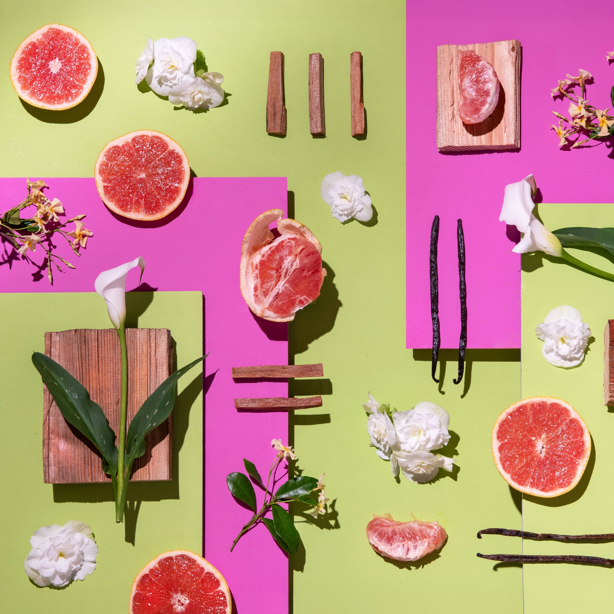 Arrangement of grapefruits, vanilla beans, and flowers on a pink and green background