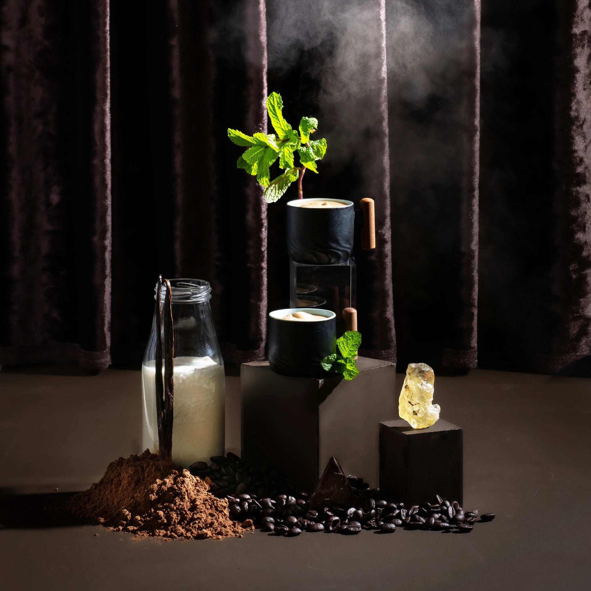 Decorative setup with vanilla beans, coffee beans, a plant, and a crystal on a dark background