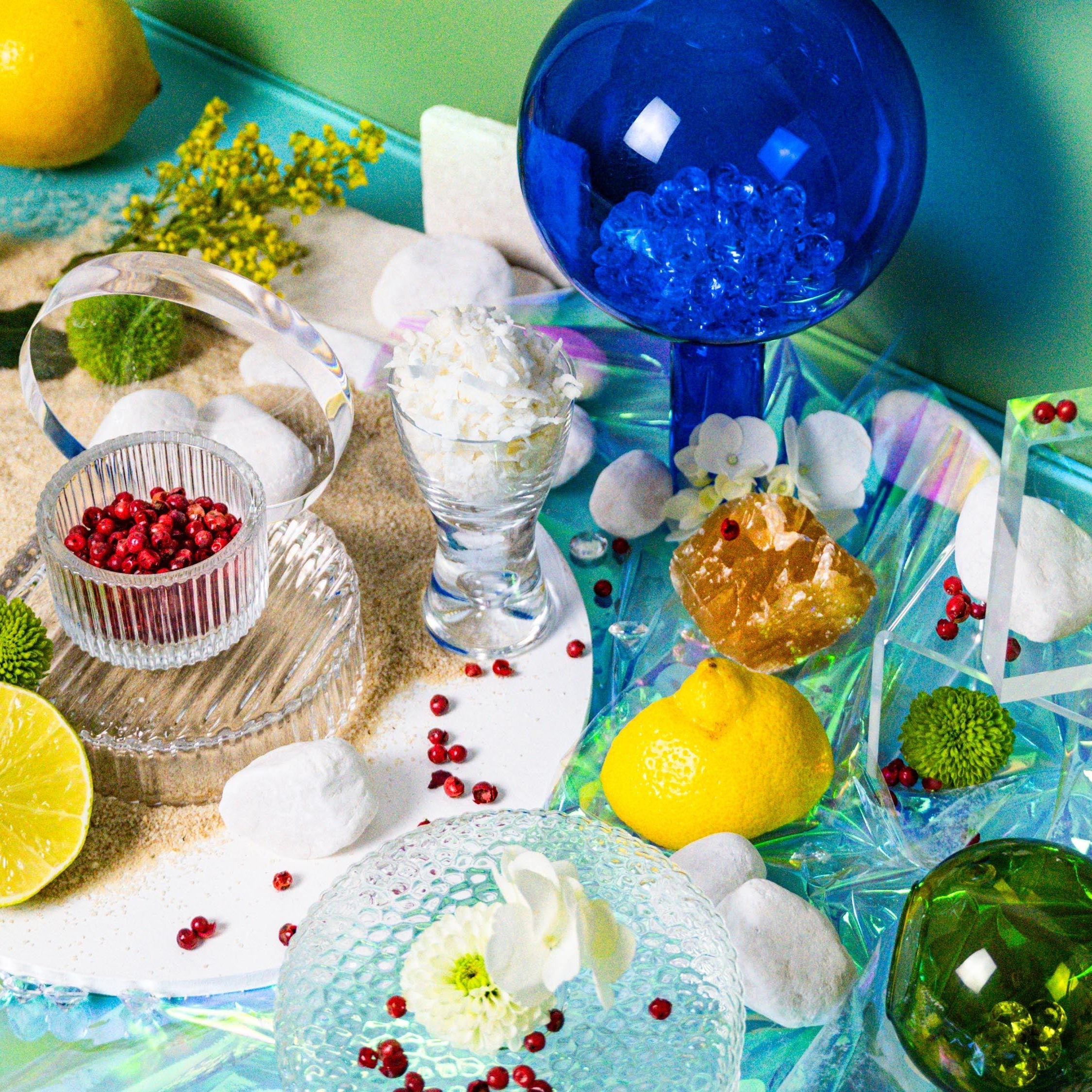 A colorful still life setup with citrus fruits, flowers, and a blue vase, representing a vibrant and summery fragrance oil theme.