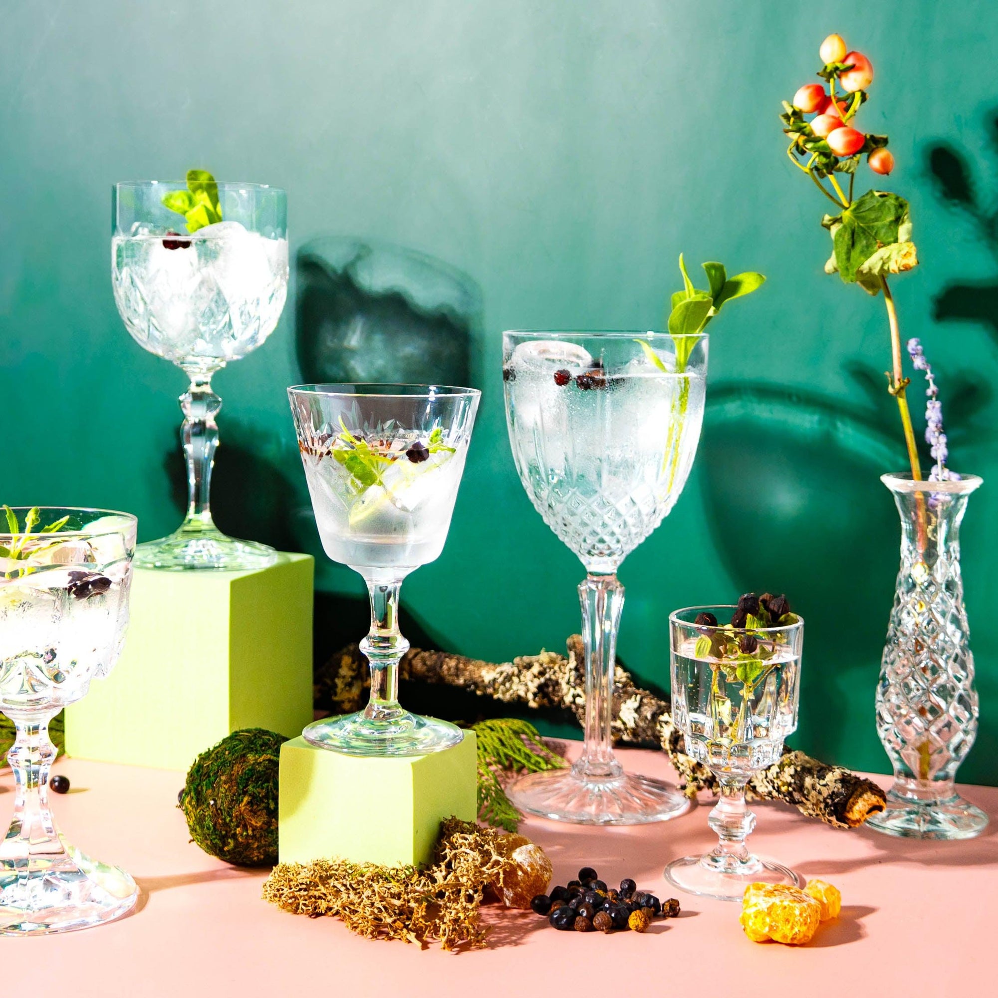 A selection of fragrance oils displayed in glass bottles, accompanied by decorative elements like flowers, herbs, and crystal glasses, set against a dual-tone background.