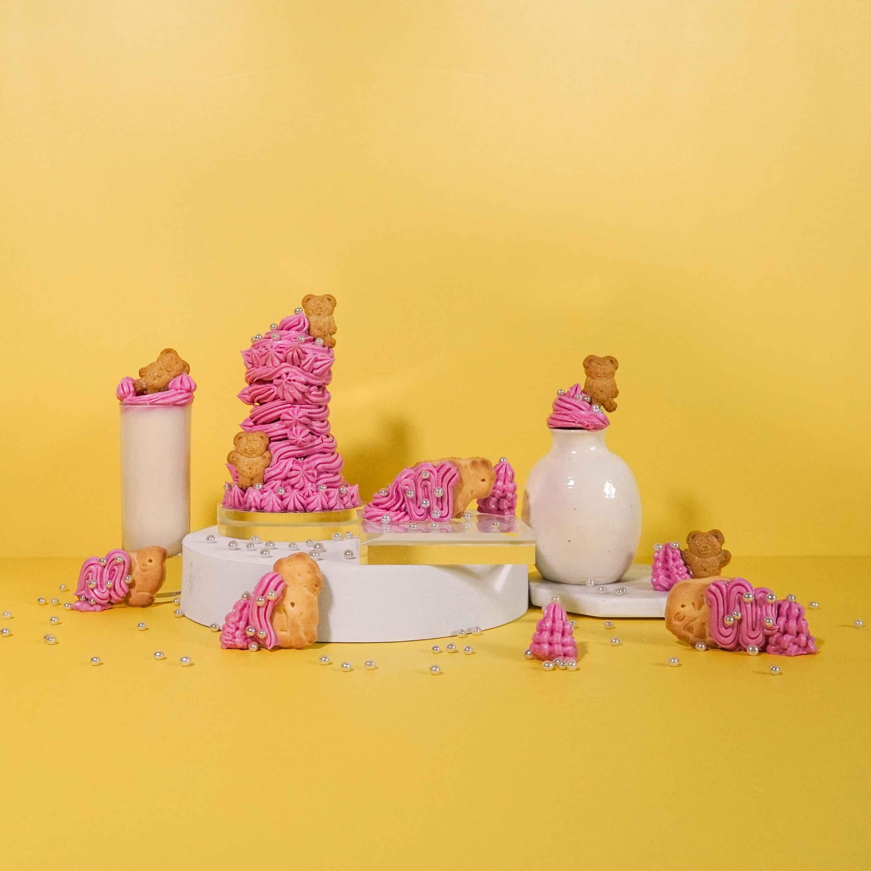A whimsical arrangement featuring pink frosted animal cookies and golden teddy bear-shaped cookies, adorned with pearl-like sugar decorations. The scene includes a tall glass of milk and a simple white ceramic vase, all placed on a sunny yellow background. Playful stacks and scattered cookies create a cheerful, nostalgic atmosphere reminiscent of childhood treats.