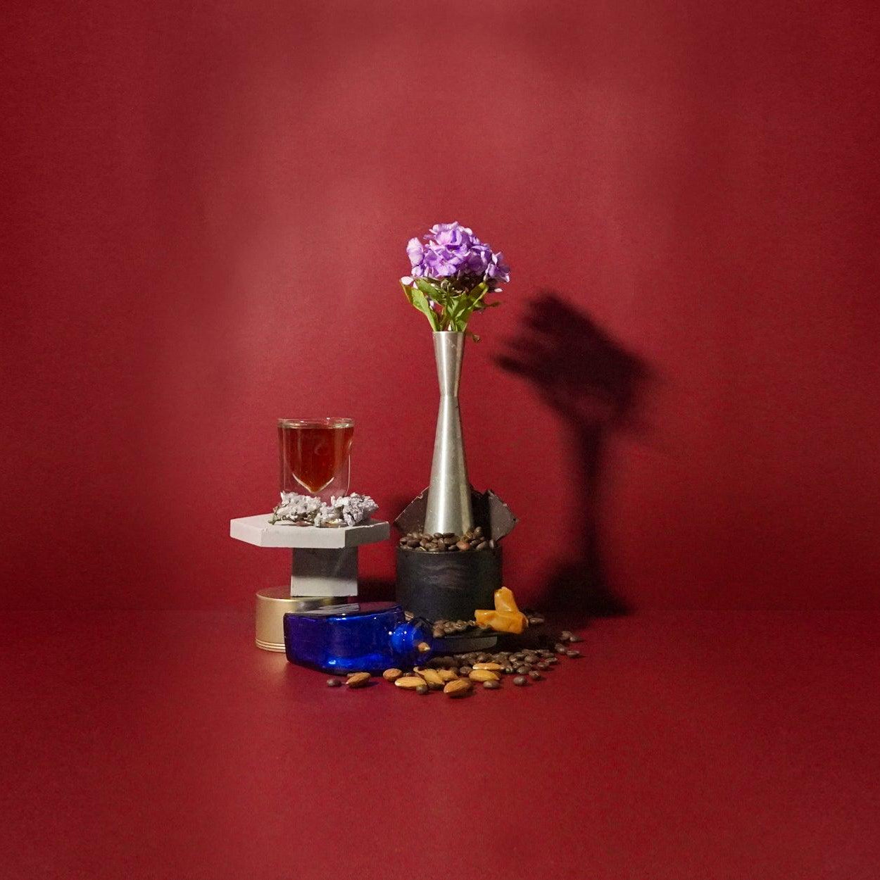 A fragrance oil product presented with a vase of flowers, coffee cup, and other thematically related items against a red background.