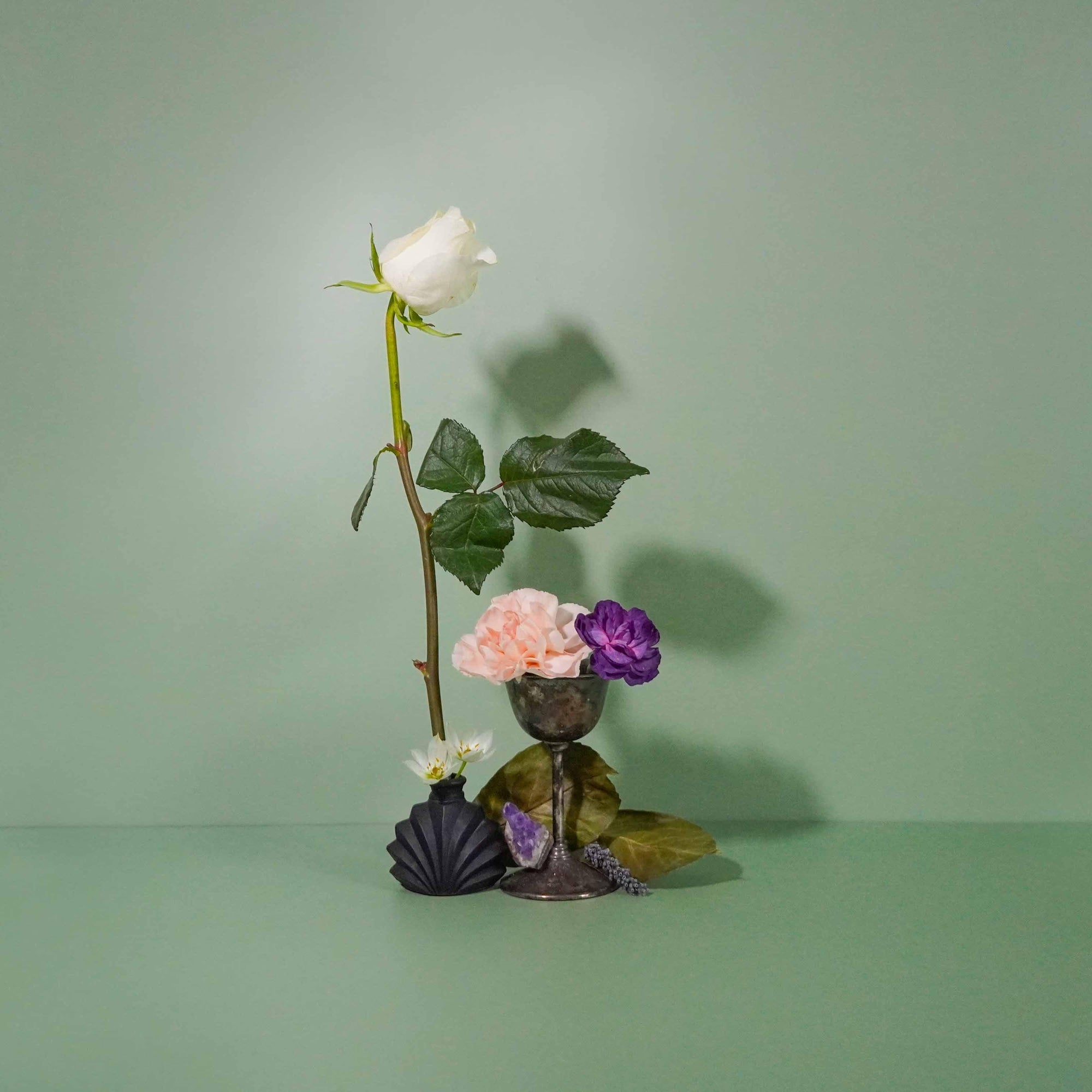 A goblet surrounded by an arrangement of fresh flowers including a white rose, pink flowers, and green leaves, against a green background.