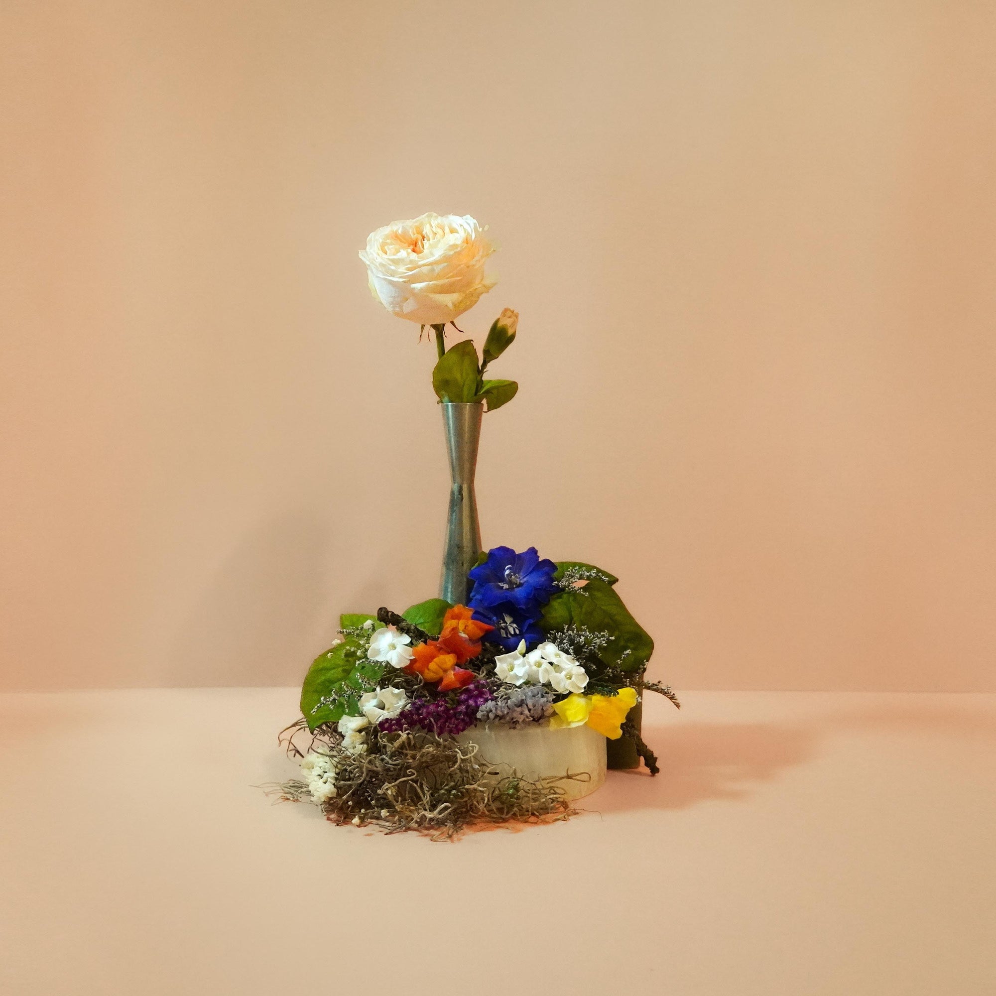 A vase with a bouquet of various flowers, including a prominent rose, arranged against a plain background.