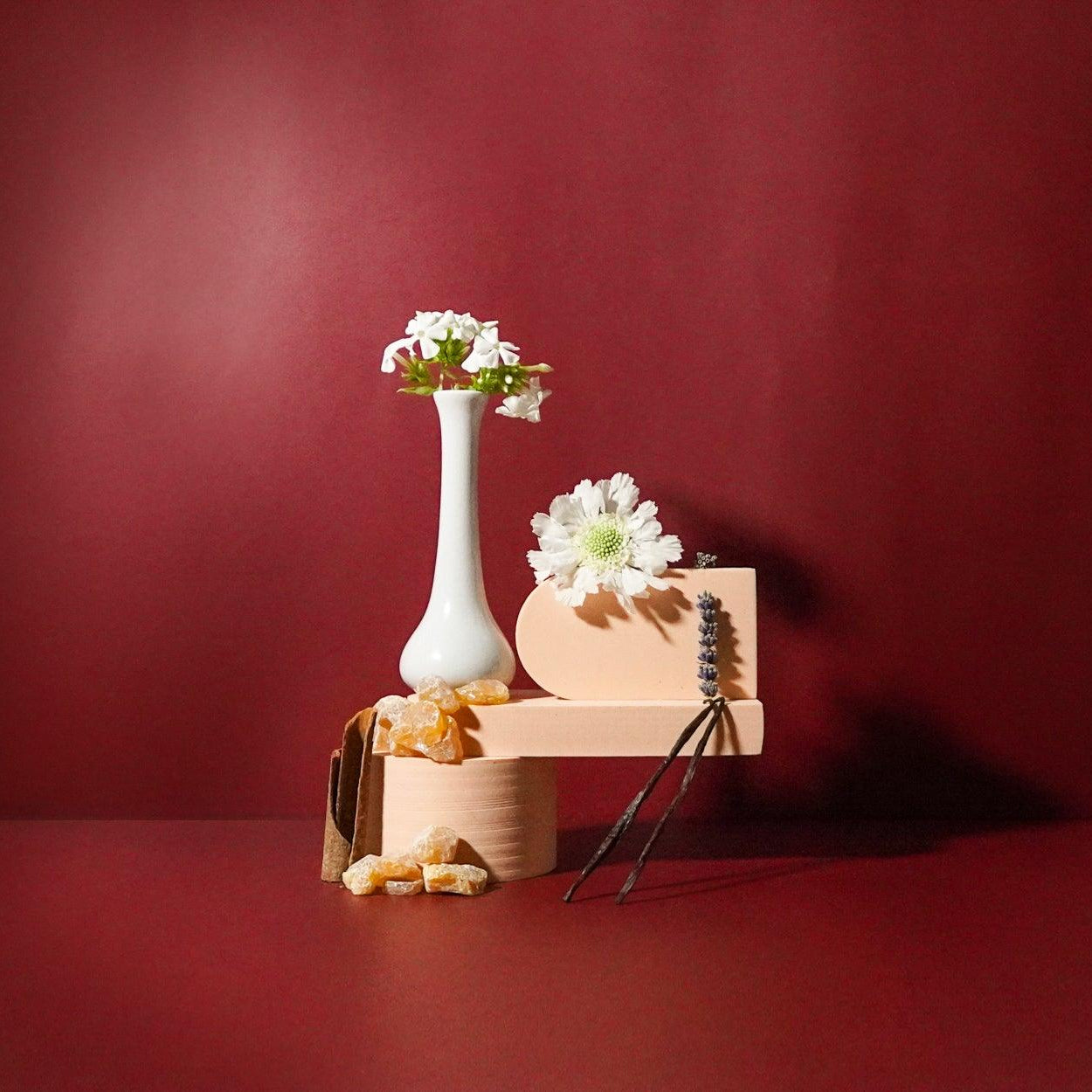 A white vase and flowers in the background, against a red backdrop.